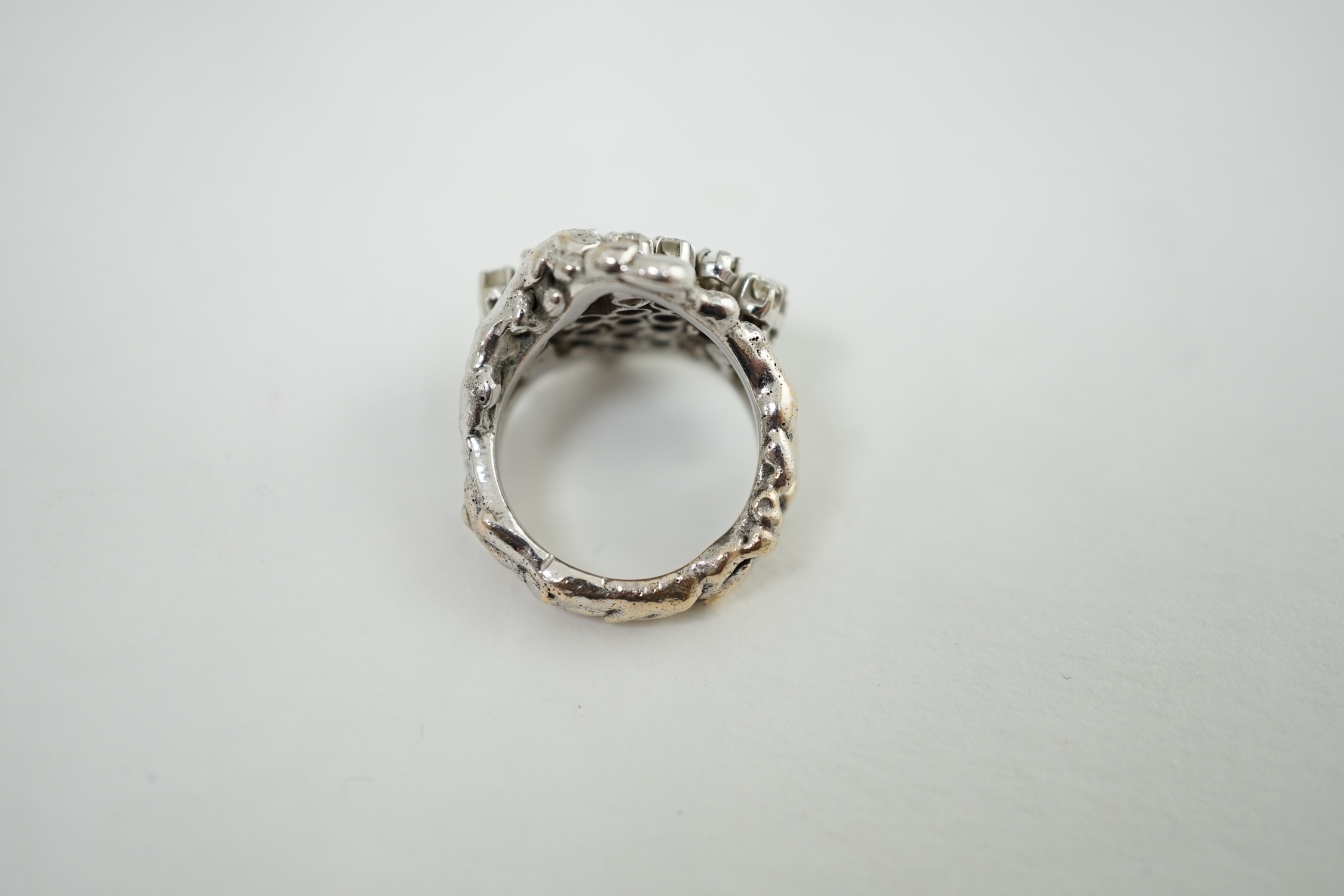 A modernist cast unmarked white metal dress ring, claw set with twenty small diamonds